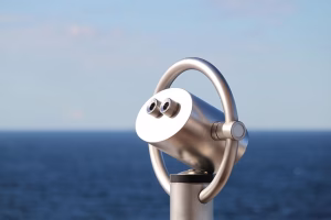 A pair of stationary binoculars on the deck of a cruise hip. Looking out into the open sea.