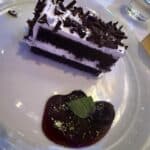 Slice of chocolate cake with whipped cream and chocolate shavings served with berry sauce and mint leaf on a white plate