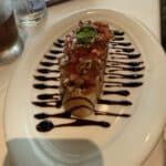 Bruschetta appetizer with diced tomatoes, basil, and balsamic glaze on a white plate at a restaurant table