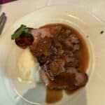 Plate with sliced roast beef topped with brown gravy, mashed potatoes, and a grilled tomato garnish on a white tablecloth