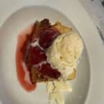 Slice of cake topped with strawberry sauce and a scoop of vanilla ice cream on a white plate during a cruise vacation meal