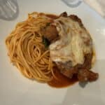 Plate of spaghetti with marinara sauce and chicken parmesan topped with melted cheese on a white tablecloth