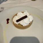 Lemon tart dessert topped with whipped cream and a chocolate stick on a white plate at a cruise ship dining table