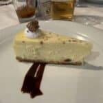 Slice of cheesecake with whipped cream and chocolate drizzle on a white plate at a cruise ship dining table