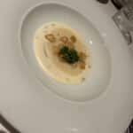 Creamy soup garnished with seared scallops and a sprig of parsley served on a white plate at a fine dining table.