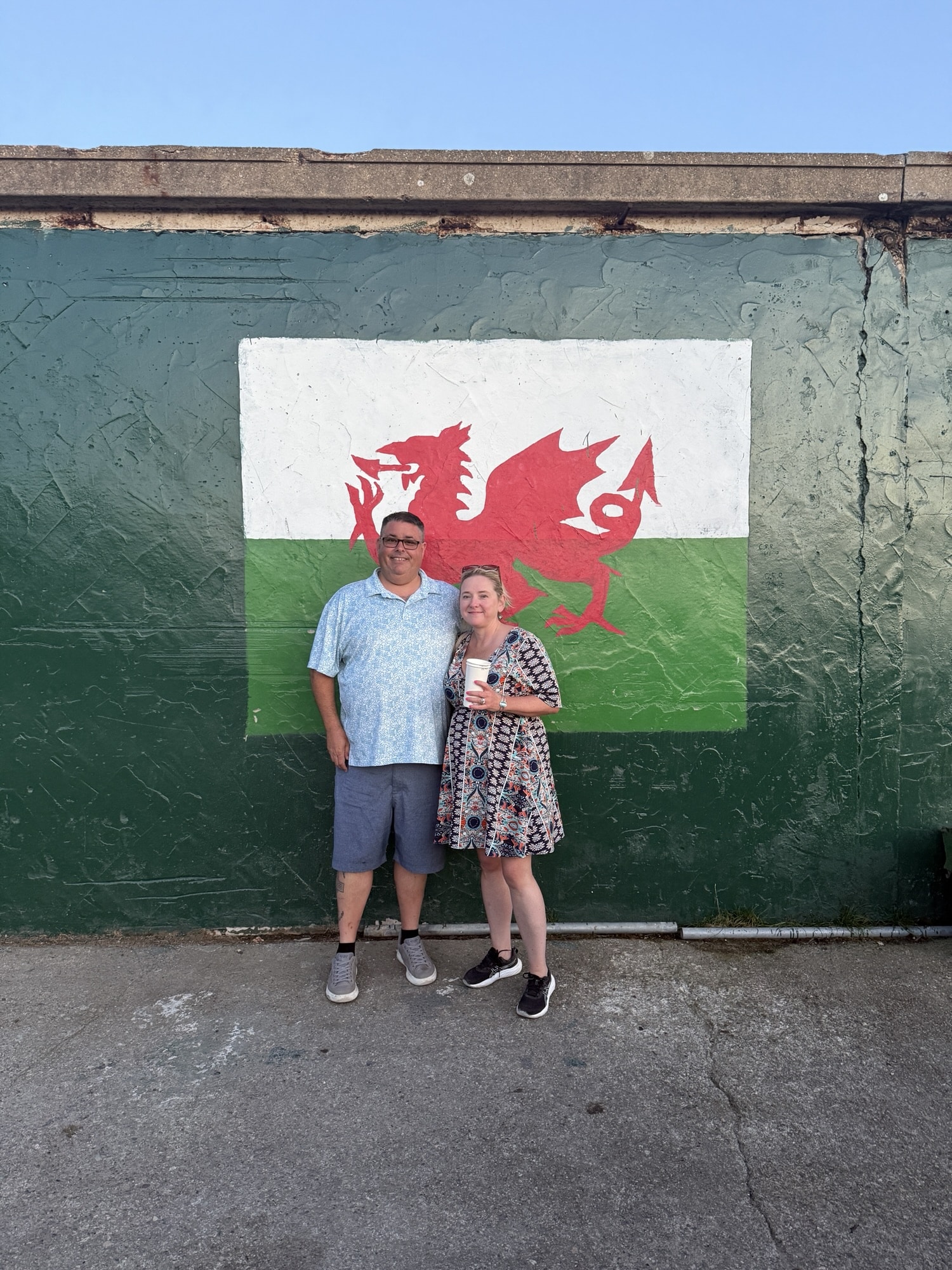 One Week in North Wales: Fairy Pools, Fighter Jets and Welsh Pubs 1 Rick and Nicole standing in front of a painted wall featuring a red dragon on a white and green background during a casual outdoor moment.